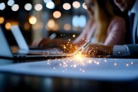 Glowing sparkles illuminate laptop keyboard in dark office setting with blurred bokeh lights background, creating magical atmosphere for business concept.