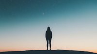 Silhouette of person standing alone on hill against gradient sky with stars at dusk. Serene minimalist landscape capturing solitude and contemplation.