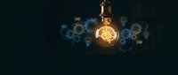 Glowing brain lightbulb with mechanical gears and innovation icons on dark background representing creativity, intelligence and breakthrough ideas.