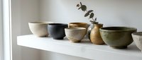 Handmade ceramic bowls in neutral earth tones arranged on white shelf with dried eucalyptus branch, showcasing artisan pottery collection for home decor and interior design styling.
