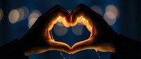 Two hands forming a glowing heart shape against a dark bokeh background, symbolizing love, romance, and connection.