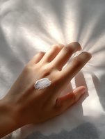 White feather delicately placed on woman's hand against soft white fabric background with natural sunlight creating ethereal shadows and rays for wellness concepts.