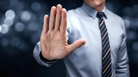Businessman in formal attire showing stop gesture with open palm against dark bokeh background, conveying authority and boundary setting.