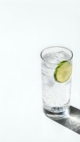 Sparkling water with ice and lime slice in a tall glass casting a dramatic shadow on a white background, refreshing summer drink concept.