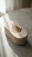 Wooden oval jewelry box with engraved fern leaf design on natural linen fabric surface in soft daylight for home decor and storage solutions.