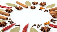 Aromatic spices frame arranged on white background with cinnamon sticks, star anise, bay leaves, cloves and chili peppers for culinary cooking recipes.