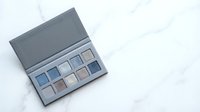 Professional makeup eyeshadow palette with neutral and blue tones on marble surface for beauty and cosmetics applications.