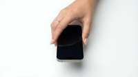Woman's hand with manicure and ring holding smartphone with blank black screen on white background, mockup for app or website display.