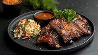 Grilled pork ribs with honey glaze served on black plate with fresh coleslaw and spicy barbecue sauce, garnished with parsley. Restaurant quality main course.