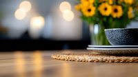 Rustic woven placemat on wooden table with blurred sunflowers and ceramic bowl in background, creating cozy home atmosphere with soft bokeh lights.