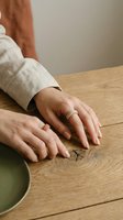 Woman hands with gold ring resting on natural wood table surface in warm neutral tones for lifestyle and wellness concepts.