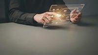 Man in business attire holding transparent digital tablet with glowing golden interface icons and data visualization, representing technology innovation and digital transformation for corporate applications.