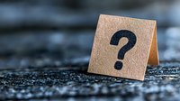 Question mark symbol on brown paper card against dark textured background, shallow depth of field creates soft blur effect for business concepts.