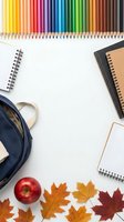 Colorful pencils arranged with school supplies, notebooks, backpack and autumn leaves on white background for back to school creative projects.