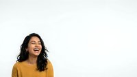 Young woman with South Asian ethnicity wearing mustard yellow sweater, smiling and looking upward against white background, expressing joy and positivity for lifestyle and portrait use.