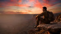 Man with backpack sitting on rocky cliff edge overlooking vast canyon landscape at sunset, contemplating nature and adventure travel destinations.