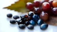 Fresh red grapes with scattered dark blue supplement capsules on white background. Health nutrition concept for dietary supplements and natural wellness.