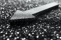 Dramatic black and white macro photograph of directional arrow covered in water droplets on textured dark surface creating abstract minimalist composition.