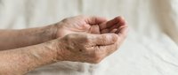 Elderly hands cupped together in prayer or meditation pose showing wrinkled skin and age spots against soft neutral background for wellness concepts.