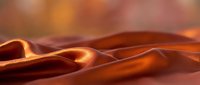 Smooth flowing copper silk fabric with warm golden highlights creating elegant waves and luxurious textile patterns for fashion and interior design projects.