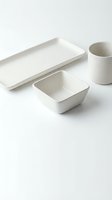 Minimalist white ceramic dinnerware set with rectangular tray, square bowl and cylindrical cup on clean background for modern kitchen and dining decor.