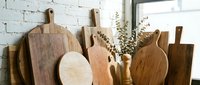 Collection of wooden cutting boards and kitchen utensils displayed against white brick wall in rustic kitchen setting for culinary preparation.