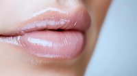Close up view of plump, glossy natural pink lips against soft blurred background, showing moisturized skin texture and subtle shine for beauty and cosmetic advertising.