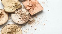 Broken cosmetic powder makeup products scattered on white surface showing various shades of foundation and face powder for beauty industry.