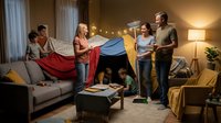 Multi-generational Caucasian family building colorful blanket fort together in cozy living room during evening bonding time at home.