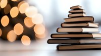 Stack of books arranged in pyramid shape with warm bokeh lights in background creating festive holiday atmosphere for reading and education concept.