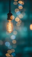 Vintage Edison bulb hanging with warm filament glow against teal bokeh background creating cozy atmospheric lighting for interior design and decor projects.