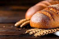 Fresh baked artisan bread loaves dusted with flour on rustic wooden background with golden wheat ears, close-up view with selective focus.