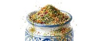 Dried herbs and spices overflowing from decorative blue and white ceramic jar with ornate pattern, isolated on white background for culinary and cooking projects.