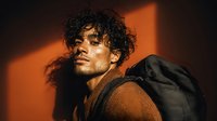 Young Hispanic man with curly hair in warm lighting with dramatic shadows, casual style portrait for lifestyle and fashion content.