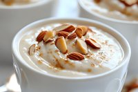 Creamy rice pudding topped with sliced almonds and cinnamon in white ceramic bowl, selective focus on dessert garnish, comfort food styling for menu photography.