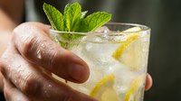 Hand holding refreshing lemon mint cocktail with ice cubes and fresh garnish for summer drinks menu and beverage photography.