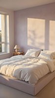 Serene bedroom with lavender walls, cream bedding, wooden nightstand with lamp, and warm sunlight streaming through window.