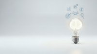 Glowing light bulb with business icons floating above on clean white background representing innovation, creativity and strategic planning concepts.