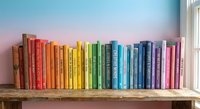 Colorful rainbow books arranged on wooden shelf creating vibrant spectrum from red to purple for home library organization and reading inspiration.