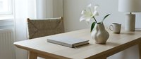 Minimalist Scandinavian home interior with wooden table, white lily in ceramic vase, notebook and mug in soft natural light.