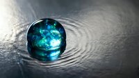 Crystal clear glass sphere with blue cosmic swirls on rippled water surface creating mesmerizing reflections and light patterns for meditation concepts.