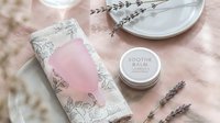 Pink floral skincare packaging with soothe balm jar and lavender sprigs on soft textile background for natural beauty branding and cosmetic product design.