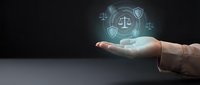 Businessman hand presenting glowing legal protection symbols with scales of justice and shield icons floating above palm on dark background.