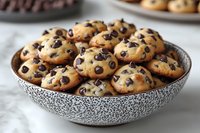 Fresh baked chocolate chip cookies in decorative speckled bowl on marble counter, warm golden brown treats with melty dark morsels for dessert or snack.