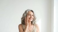 Confident mature woman with gray hair smiling warmly in beige top against neutral background. Natural aging, wellness lifestyle concept for health campaigns.