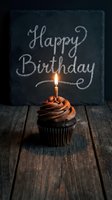 Chocolate cupcake with lit candle on rustic wood, Happy Birthday chalkboard sign behind, warm moody celebration concept.