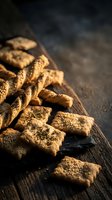 Savory crackers with sesame seeds and herbs arranged on dark wooden board, ideal for food styling, culinary content, and recipe photography.