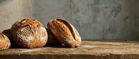 Freshly baked artisan bread loaves with golden crusts on rustic wooden table against textured concrete wall background for bakery and food photography.