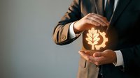 Professional businessman in suit protecting glowing plant icon with hands symbolizing environmental protection, sustainability and green business growth.