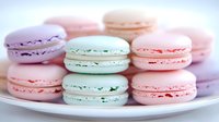 Sweet pastel macarons in pink, mint green, and lavender arranged on white plate. French meringue sandwich cookies with cream filling for dessert or cafe menu.